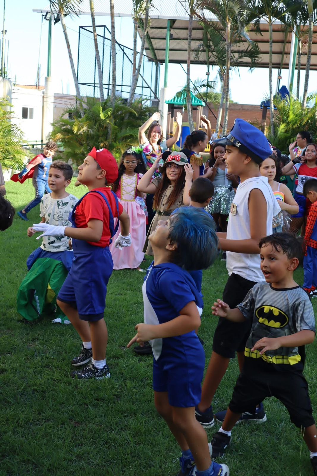 Crianças fantasiadas em atividade coletiva na área verde do Lógica
